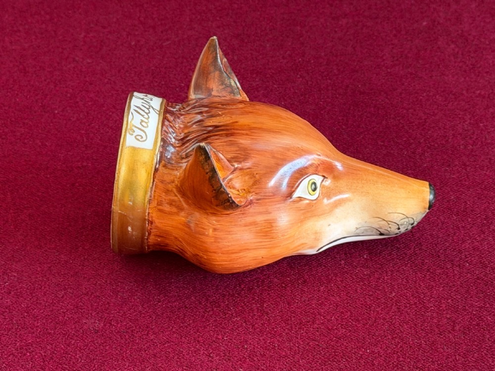 An antique porcelain stirrup cup moulded in the form of a fox head with hand-painted details and a gilded rim inscribed with Tallyho. View II