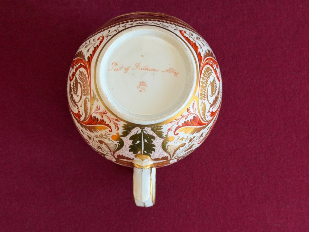 A Regency era Derby porcelain jug featuring a hand-painted landscape panel framed by gold leaf cartouche details and coral-tinted scrollwork. View III