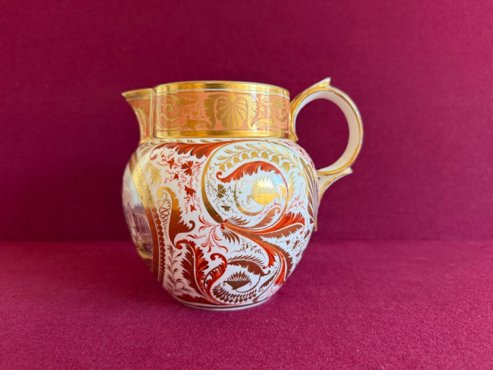A Regency era Derby porcelain jug featuring a hand-painted landscape panel framed by gold leaf cartouche details and coral-tinted scrollwork. View IV