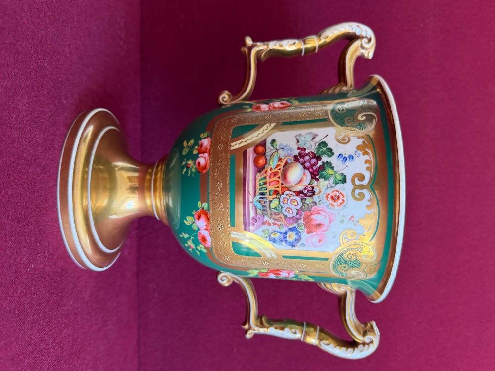 A two-handled green porcelain cup decorated with gold gilding and a hand-painted fruit and floral cartouche on a pedestal foot. View V