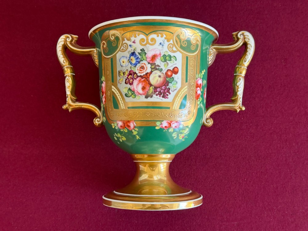 A two-handled green porcelain cup decorated with gold gilding and a hand-painted fruit and floral cartouche on a pedestal foot. View VII