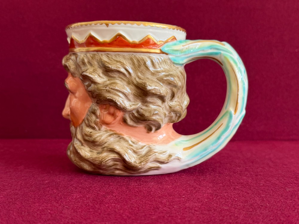 An 18th-century Derby porcelain mug sculpted in the shape of Neptunes head with a painted beard, skin tones, and a red and gold crown rim. View II