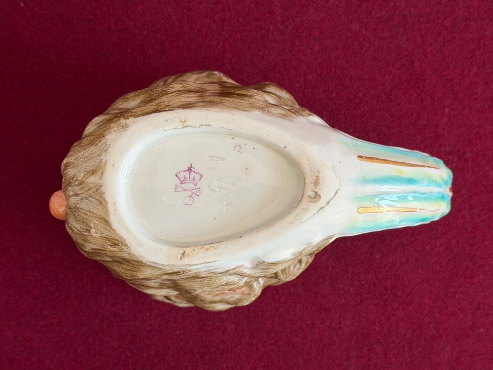 An 18th-century Derby porcelain mug sculpted in the shape of Neptunes head with a painted beard, skin tones, and a red and gold crown rim. View V