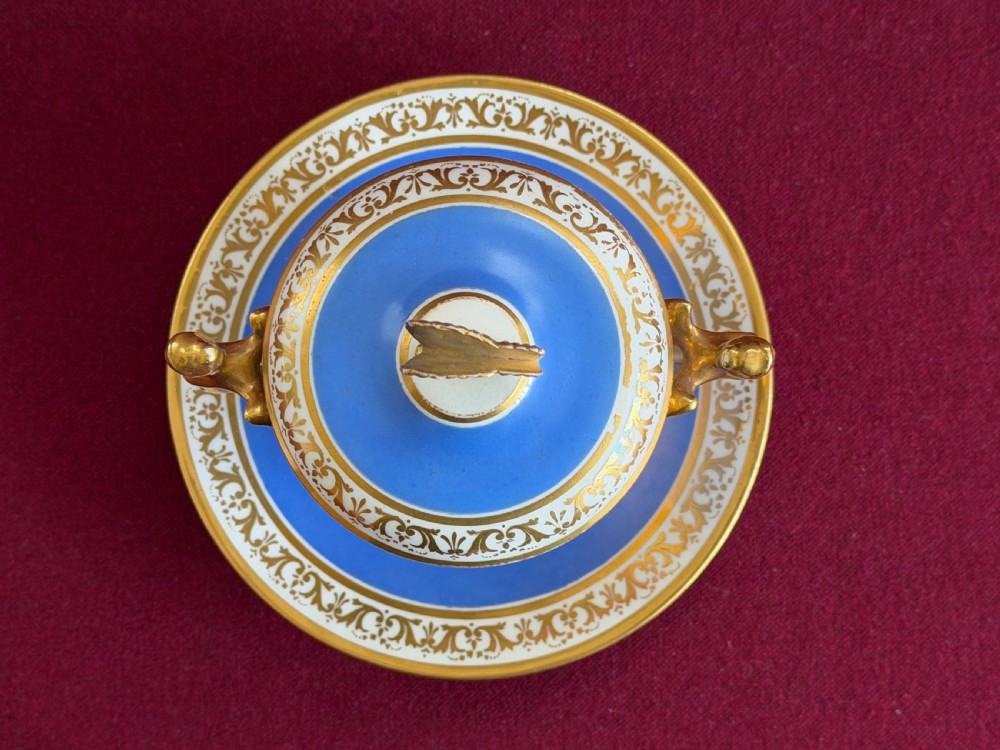 An antique Regency porcelain chocolate cup, cover, and saucer decorated with cobalt blue panels, rich gilding, winged caryatid handles, and a central hand-painted floral bouquet. View V
