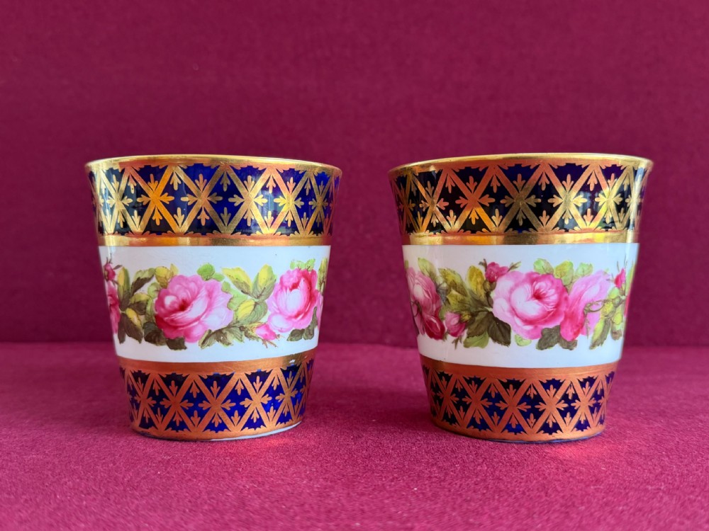 A pair of tapered porcelain beakers featuring a hand-painted floral rose band positioned between cobalt blue borders decorated with gold lattice gilding. View II