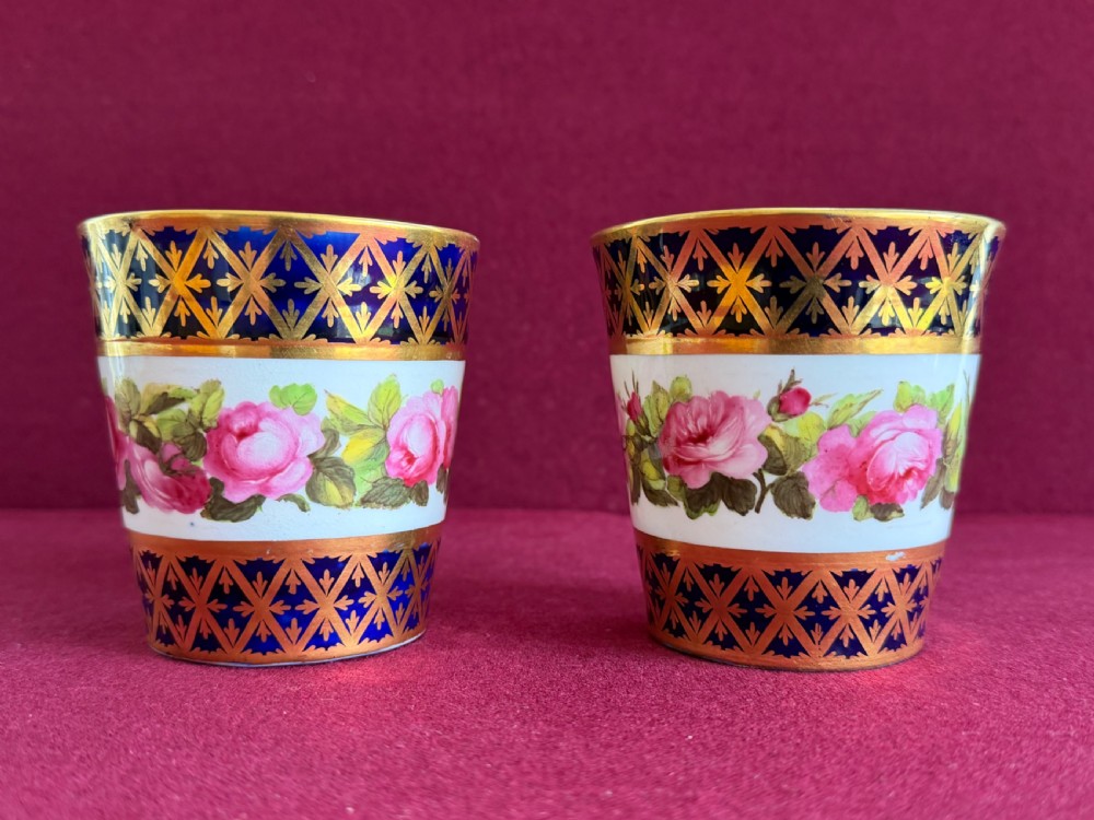 A pair of tapered porcelain beakers featuring a hand-painted floral rose band positioned between cobalt blue borders decorated with gold lattice gilding. View III
