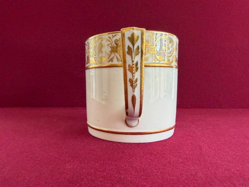 A cylindrical white porcelain porter mug featuring a hand-painted landscape scene framed by ornate gilded scrollwork and classical motifs. View III