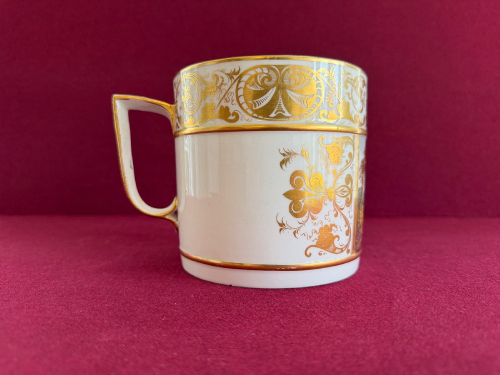 A cylindrical white porcelain porter mug featuring a hand-painted landscape scene framed by ornate gilded scrollwork and classical motifs. View IV