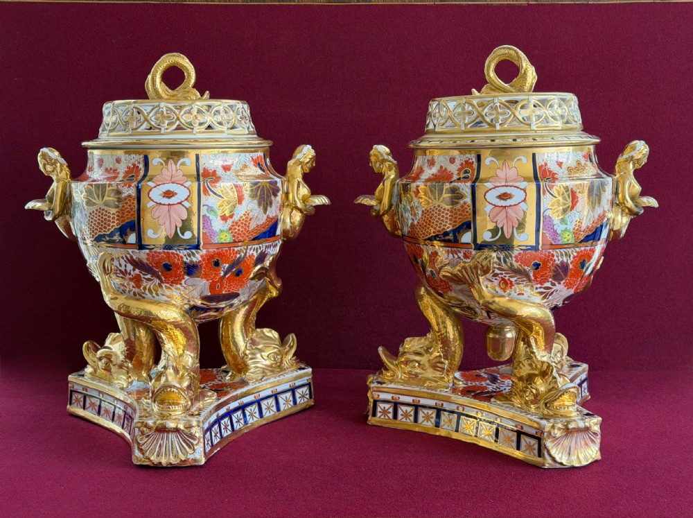 A pair of ornate Regency porcelain ice pails with Imari enamel patterns in orange, blue, and gold, resting on gilded dolphin supports.
