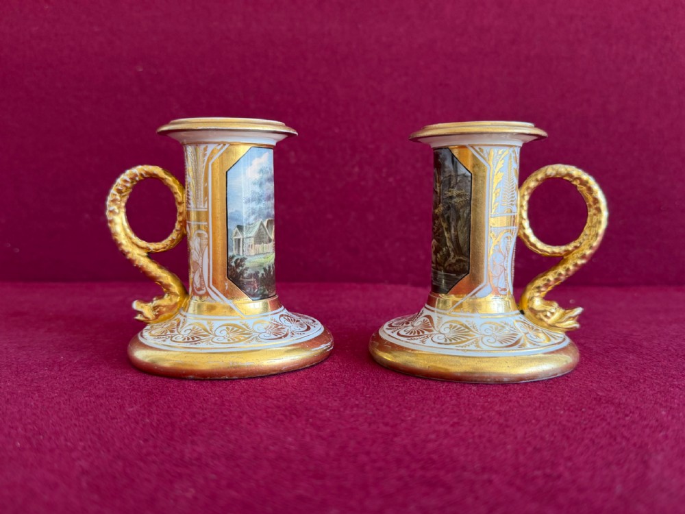 A pair of early nineteenth-century porcelain candlesticks featuring hand-painted landscape scenes on the shafts and detailed gilding on the bases. View II
