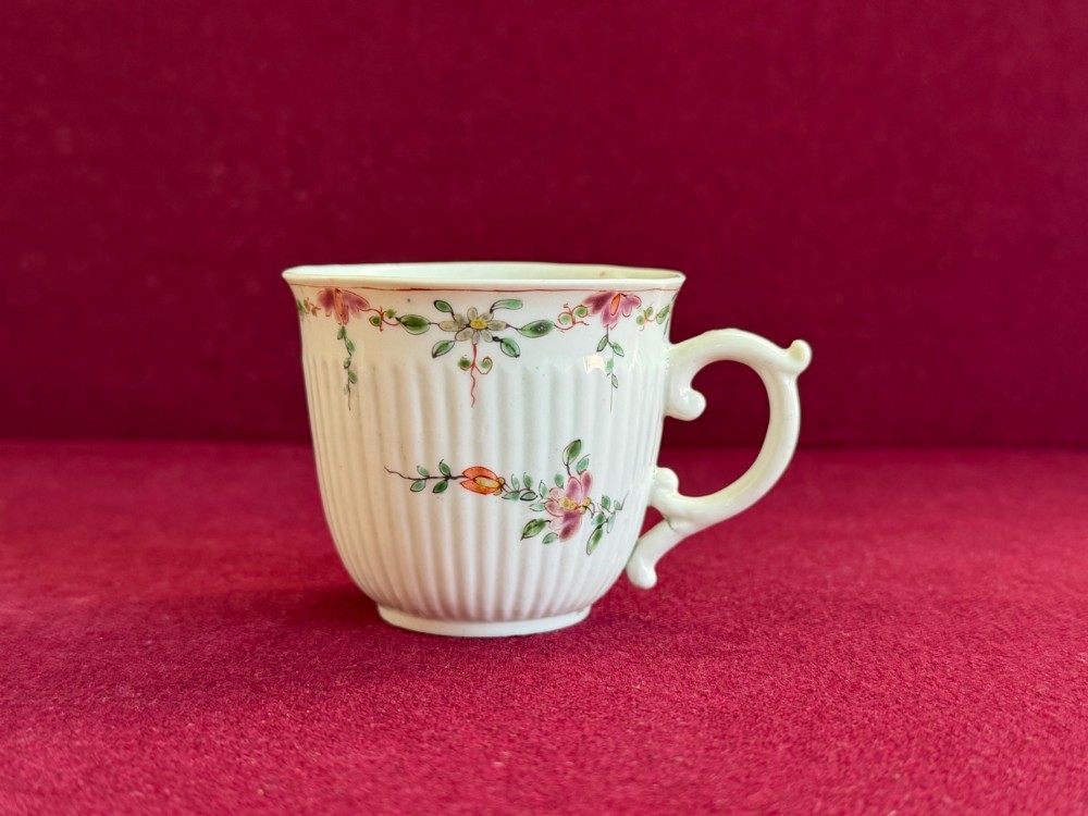 A mid-18th-century white soft-paste porcelain coffee cup featuring vertical reeding, a Rococo scroll handle, and hand-painted floral sprigs.
