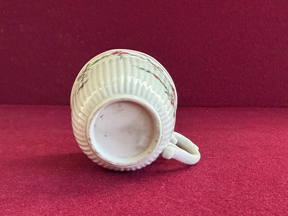 A mid-18th-century white soft-paste porcelain coffee cup featuring vertical reeding, a Rococo scroll handle, and hand-painted floral sprigs. View V