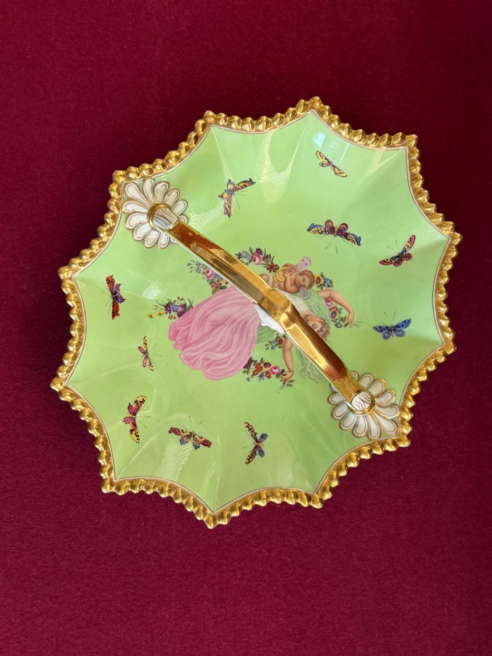 An apple green lobed porcelain basket with a gold overhead handle, gadrooned gilded border, and hand-painted central vignette of a classical figure and butterflies. View II