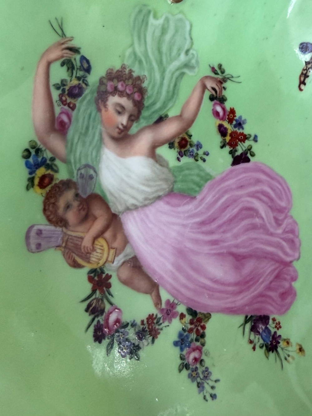 An apple green lobed porcelain basket with a gold overhead handle, gadrooned gilded border, and hand-painted central vignette of a classical figure and butterflies. View IV