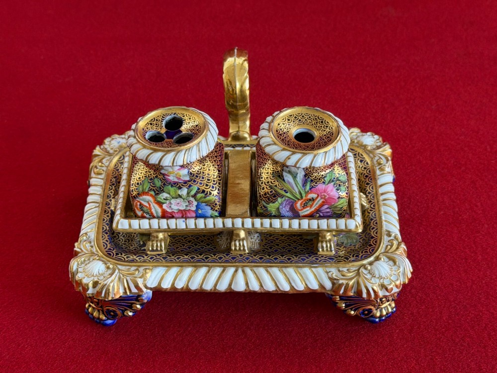 A Regency porcelain inkstand featuring elaborate gilding over a dark blue ground with polychrome floral panels and a central handle.