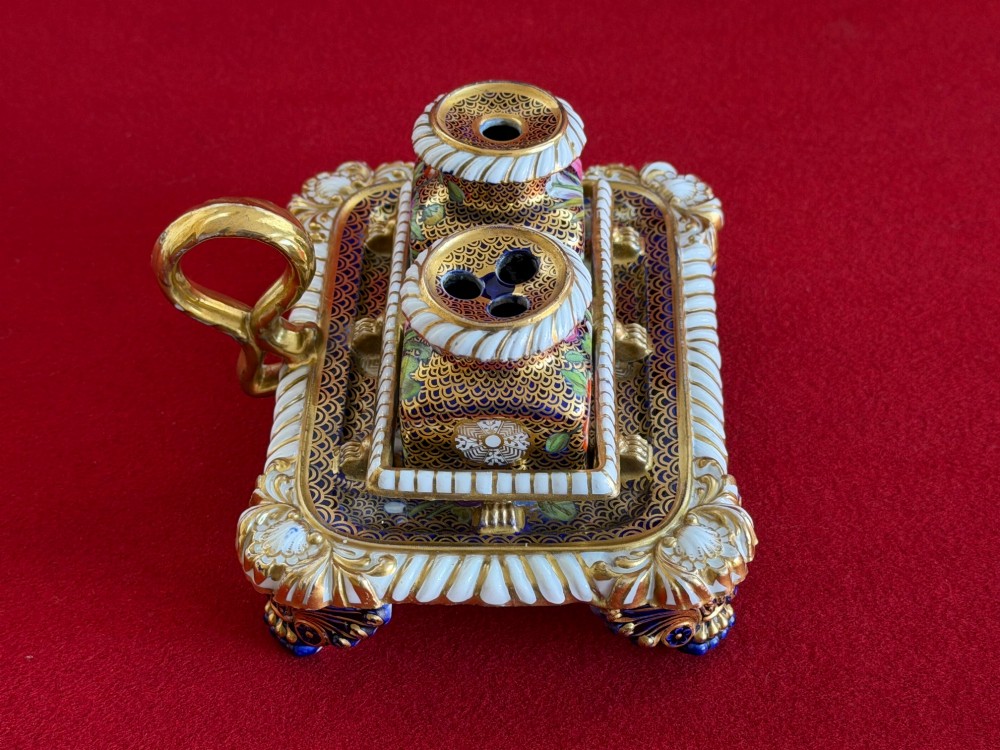 A Regency porcelain inkstand featuring elaborate gilding over a dark blue ground with polychrome floral panels and a central handle. View II