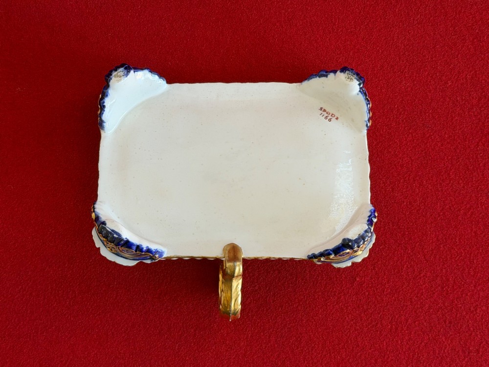 A Regency porcelain inkstand featuring elaborate gilding over a dark blue ground with polychrome floral panels and a central handle. View VI