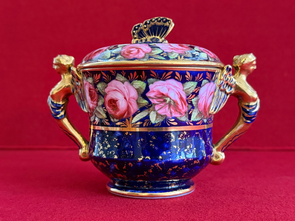 An antique Regency period porcelain covered chocolate cup with matching saucer, decorated in cobalt blue and hand-painted pink roses with winged figure handles and a butterfly finial. View III