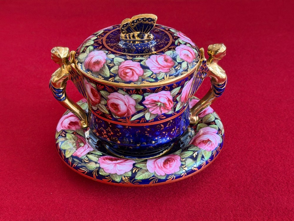 An antique Regency period porcelain covered chocolate cup with matching saucer, decorated in cobalt blue and hand-painted pink roses with winged figure handles and a butterfly finial. View VIII
