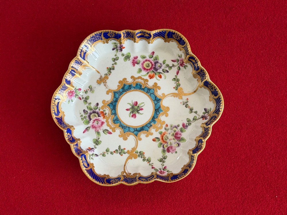 A fluted, barrel-shaped First Period Worcester porcelain teapot with matching stand, featuring hand-painted floral motifs, cobalt blue borders with gilt detailing, and a floral finial on the lid. View III