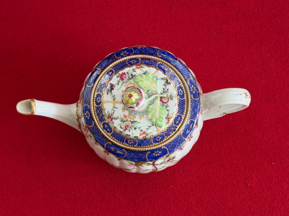 A fluted, barrel-shaped First Period Worcester porcelain teapot with matching stand, featuring hand-painted floral motifs, cobalt blue borders with gilt detailing, and a floral finial on the lid. View IV
