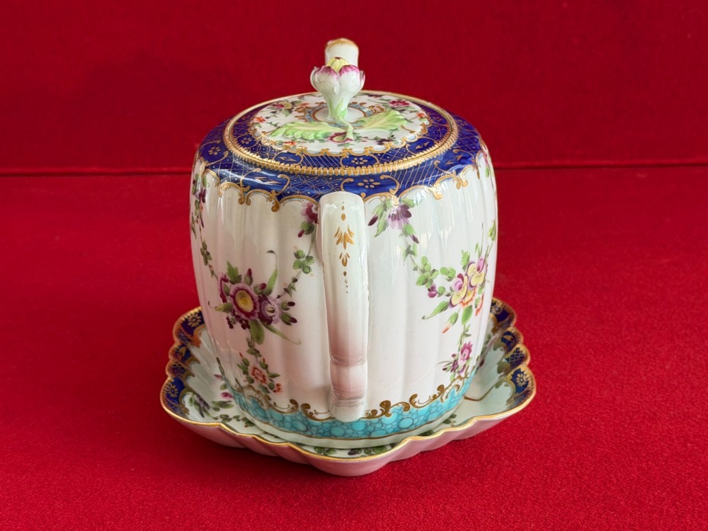 A fluted, barrel-shaped First Period Worcester porcelain teapot with matching stand, featuring hand-painted floral motifs, cobalt blue borders with gilt detailing, and a floral finial on the lid. View V