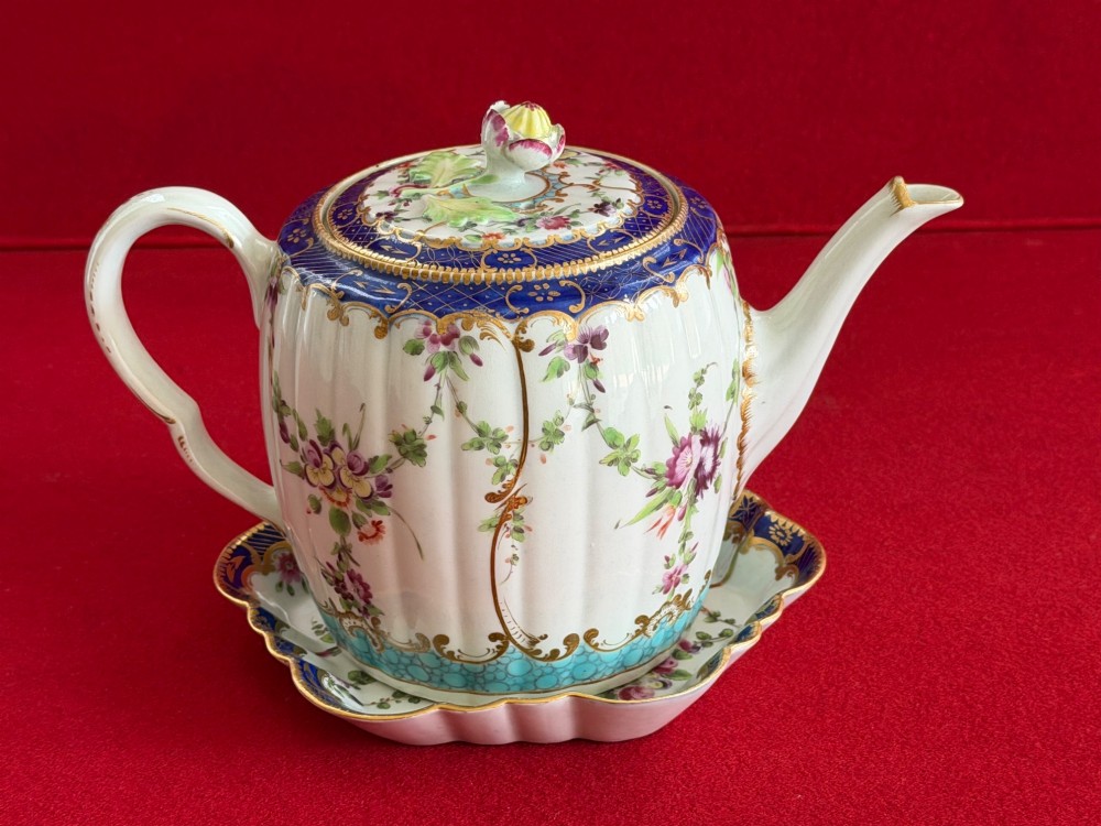 A fluted, barrel-shaped First Period Worcester porcelain teapot with matching stand, featuring hand-painted floral motifs, cobalt blue borders with gilt detailing, and a floral finial on the lid. View VI