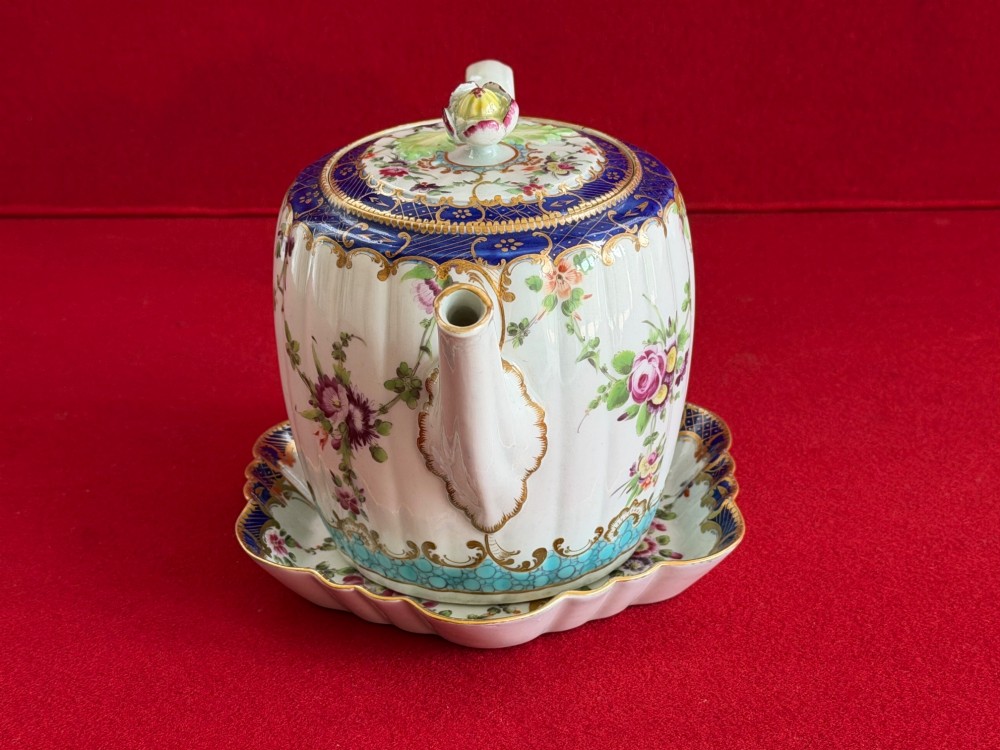 A fluted, barrel-shaped First Period Worcester porcelain teapot with matching stand, featuring hand-painted floral motifs, cobalt blue borders with gilt detailing, and a floral finial on the lid. View VII