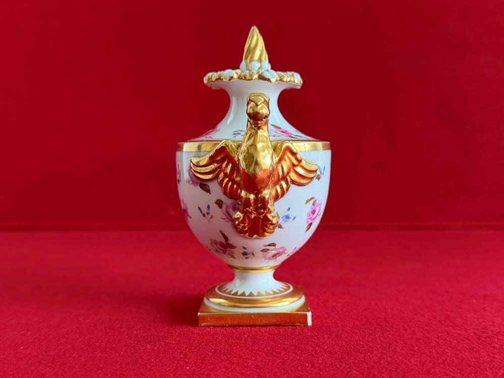 A Regency porcelain rose water sprinkler decorated with pink painted floral sprigs, a gilded spout, a scroll handle, and a square gilded plinth base. View IV