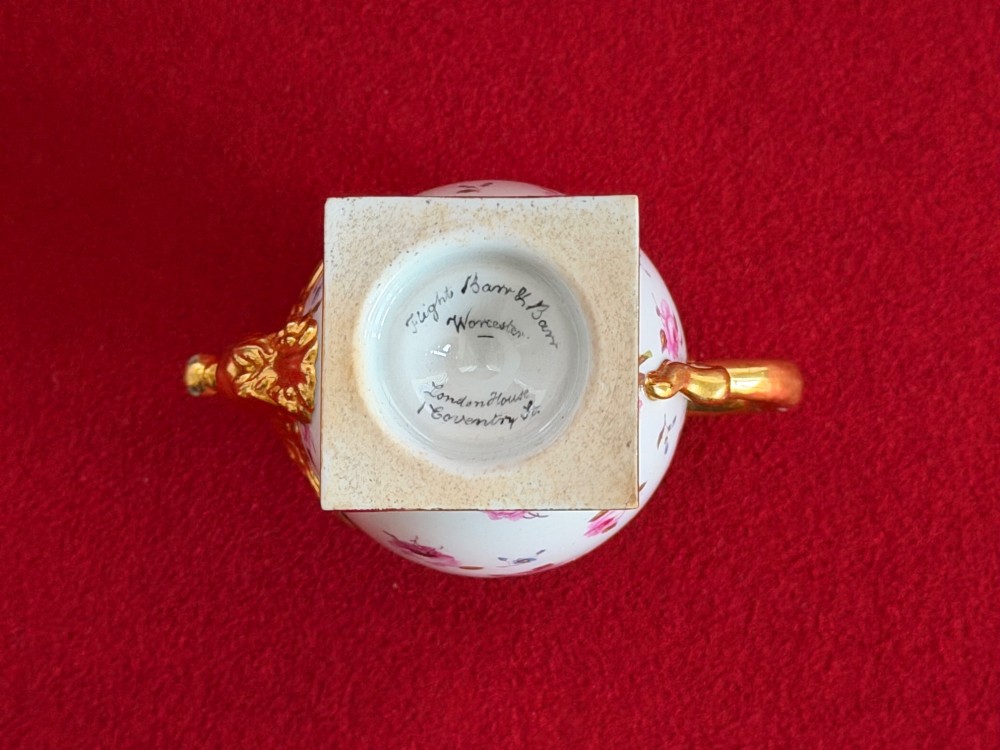 A Regency porcelain rose water sprinkler decorated with pink painted floral sprigs, a gilded spout, a scroll handle, and a square gilded plinth base. View V