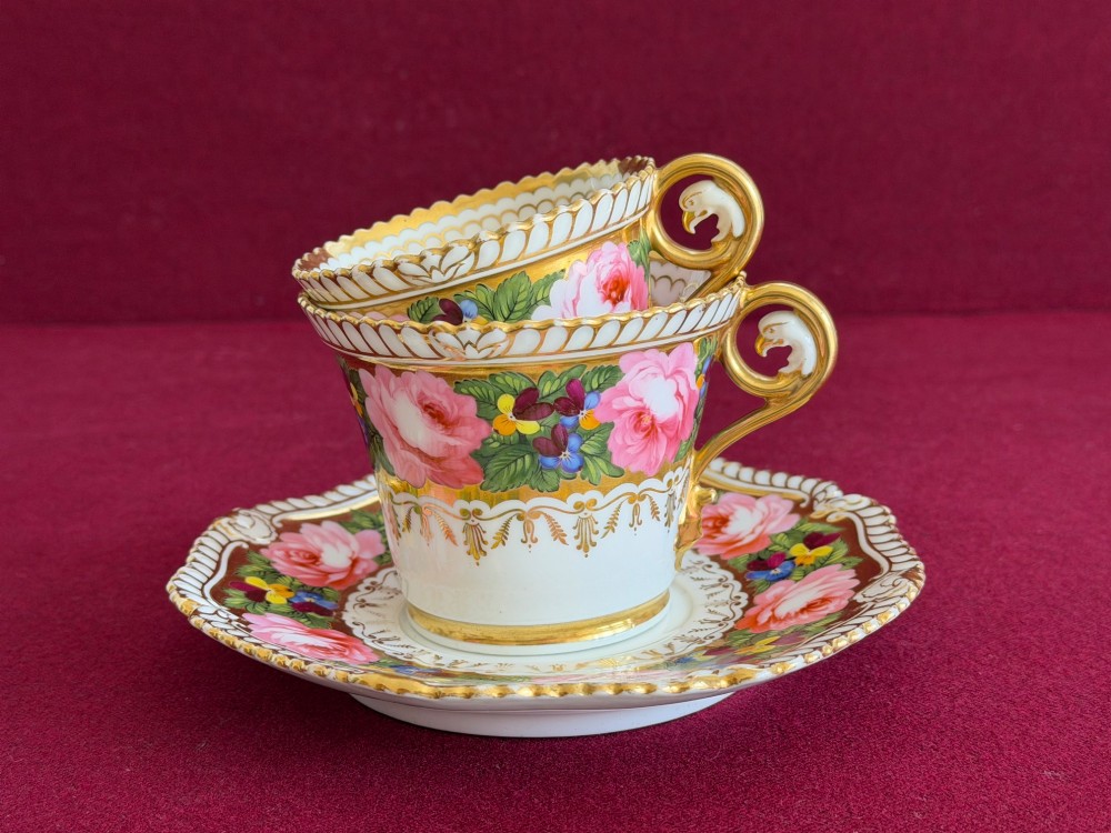 An antique Regency Chamberlain Worcester porcelain trio featuring hand-painted pink roses, pansies, rich gilded borders, and eagle-head handle terminals.