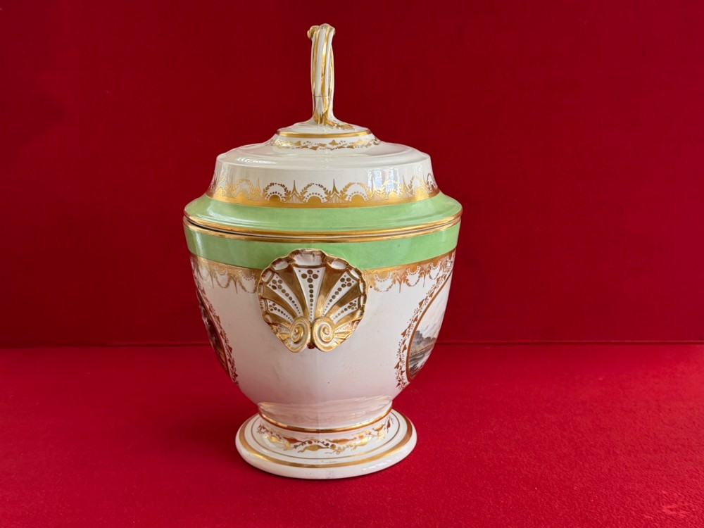 A late 18th-century Derby porcelain ice pail with twin scroll handles, a looping lid finial, an apple-green band, gold gilding, and a central oval landscape painting. View II