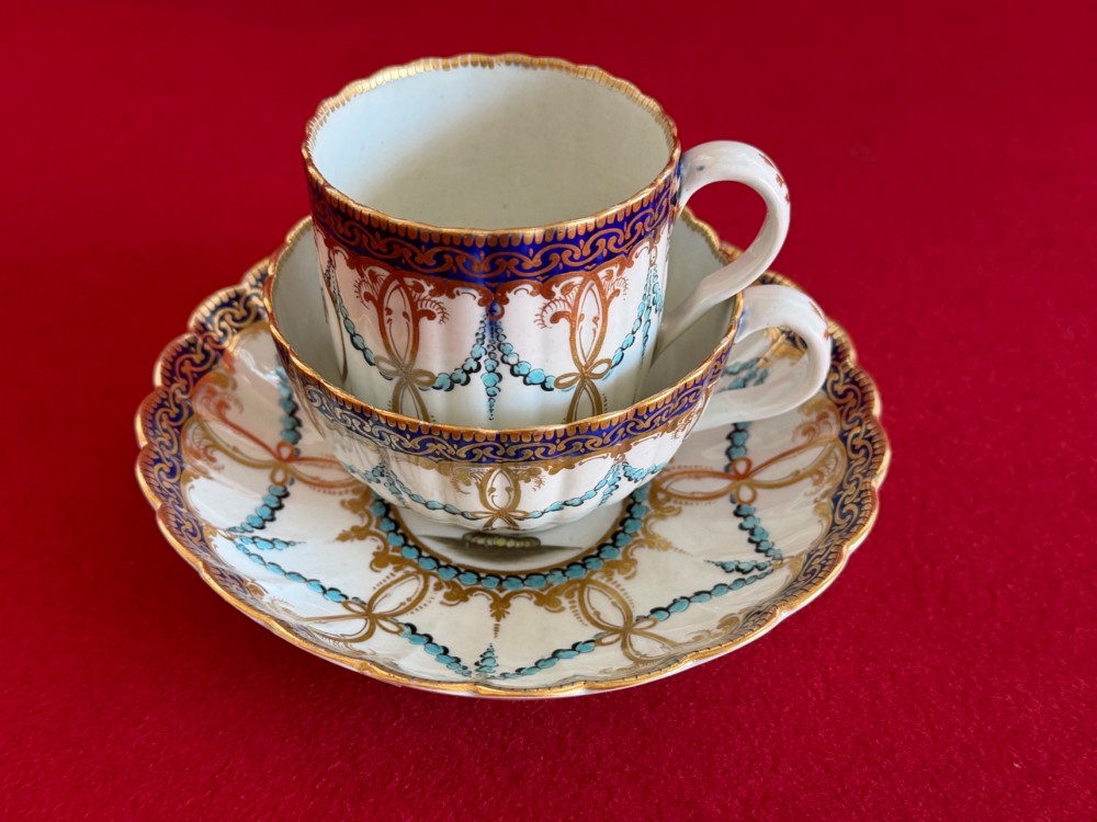 An 18th-century Worcester porcelain trio comprising a teacup, coffee cup, and saucer decorated with fluted moulding, blue swags, Classical urn motifs, and gold leaf gilding. View V