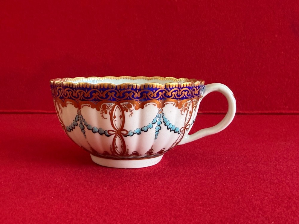 An 18th-century Worcester porcelain trio comprising a teacup, coffee cup, and saucer decorated with fluted moulding, blue swags, Classical urn motifs, and gold leaf gilding. View VII