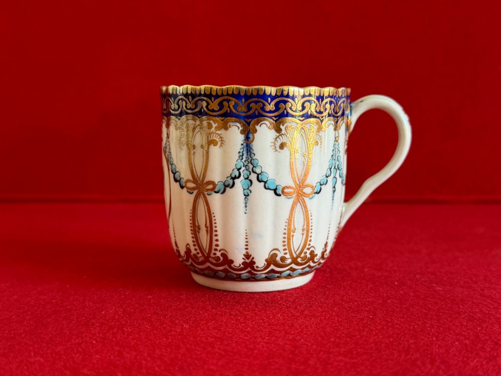 An 18th-century Worcester porcelain trio comprising a teacup, coffee cup, and saucer decorated with fluted moulding, blue swags, Classical urn motifs, and gold leaf gilding. View VIII