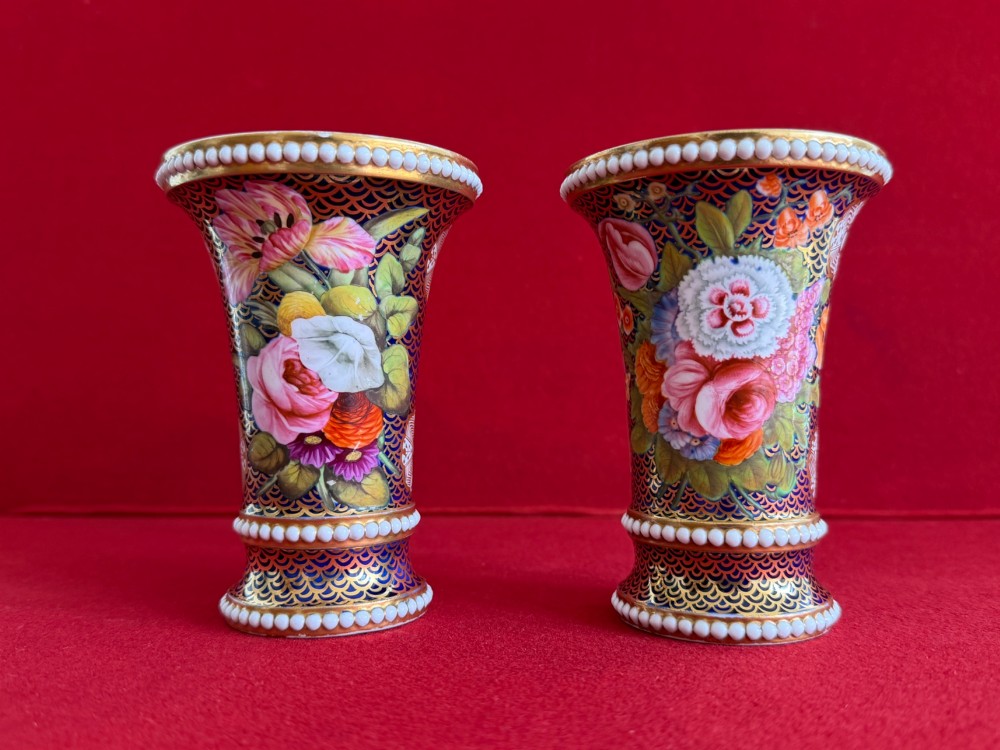 A pair of flared Regency Spode porcelain spill vases decorated with dark blue gilded fishscale patterns, colourful hand-painted floral panels, and white beaded borders.