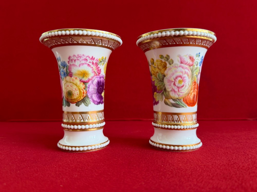 A pair of flared white antique porcelain spill vases painted with colourful floral bouquets and trimmed with gilded geometric borders and beaded rims.