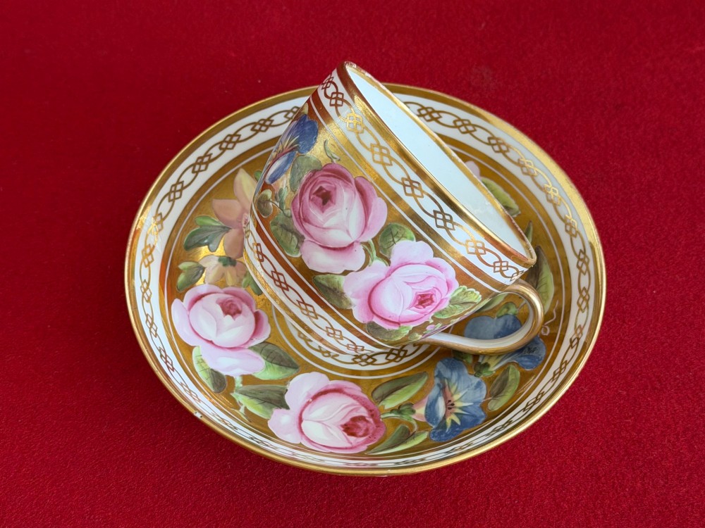 A Regency John Rose Coalport porcelain trio comprising a teacup, coffee can, and matching saucer featuring hand-painted pink roses on a gold ground. View IV