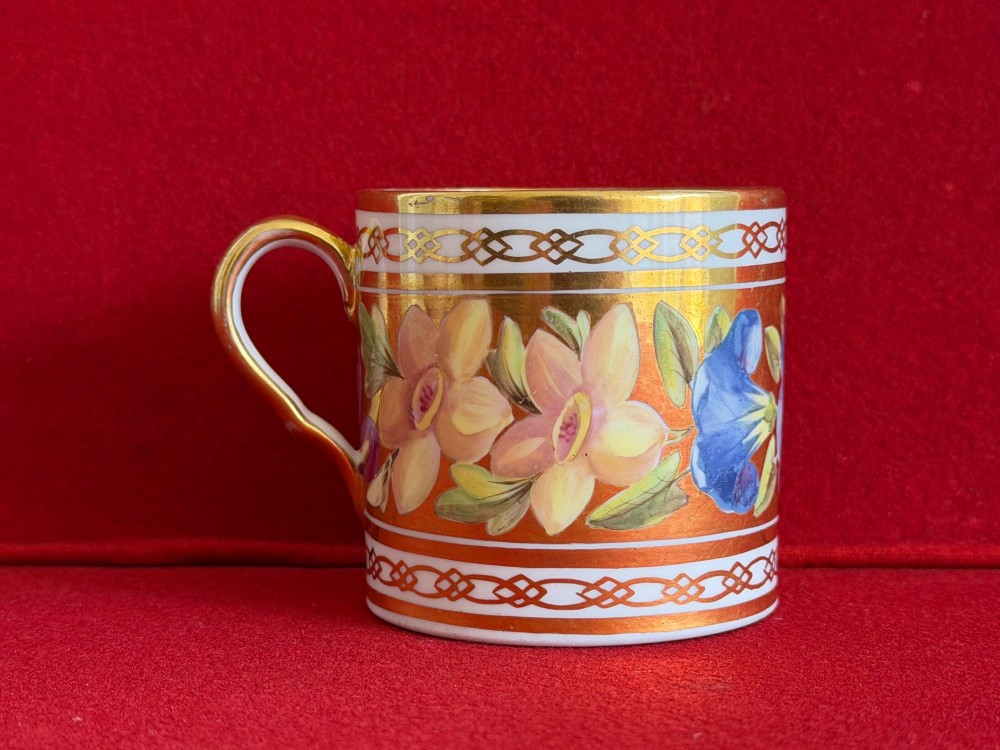 A Regency John Rose Coalport porcelain trio comprising a teacup, coffee can, and matching saucer featuring hand-painted pink roses on a gold ground. View V