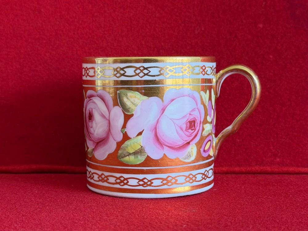 A Regency John Rose Coalport porcelain trio comprising a teacup, coffee can, and matching saucer featuring hand-painted pink roses on a gold ground. View VI