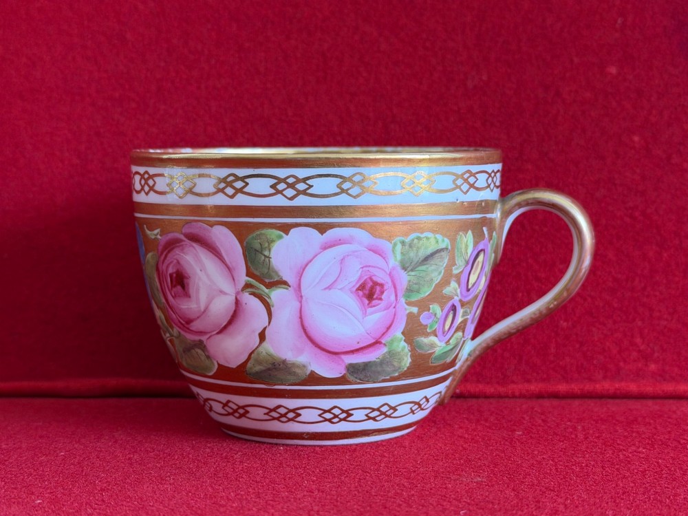 A Regency John Rose Coalport porcelain trio comprising a teacup, coffee can, and matching saucer featuring hand-painted pink roses on a gold ground. View VIII