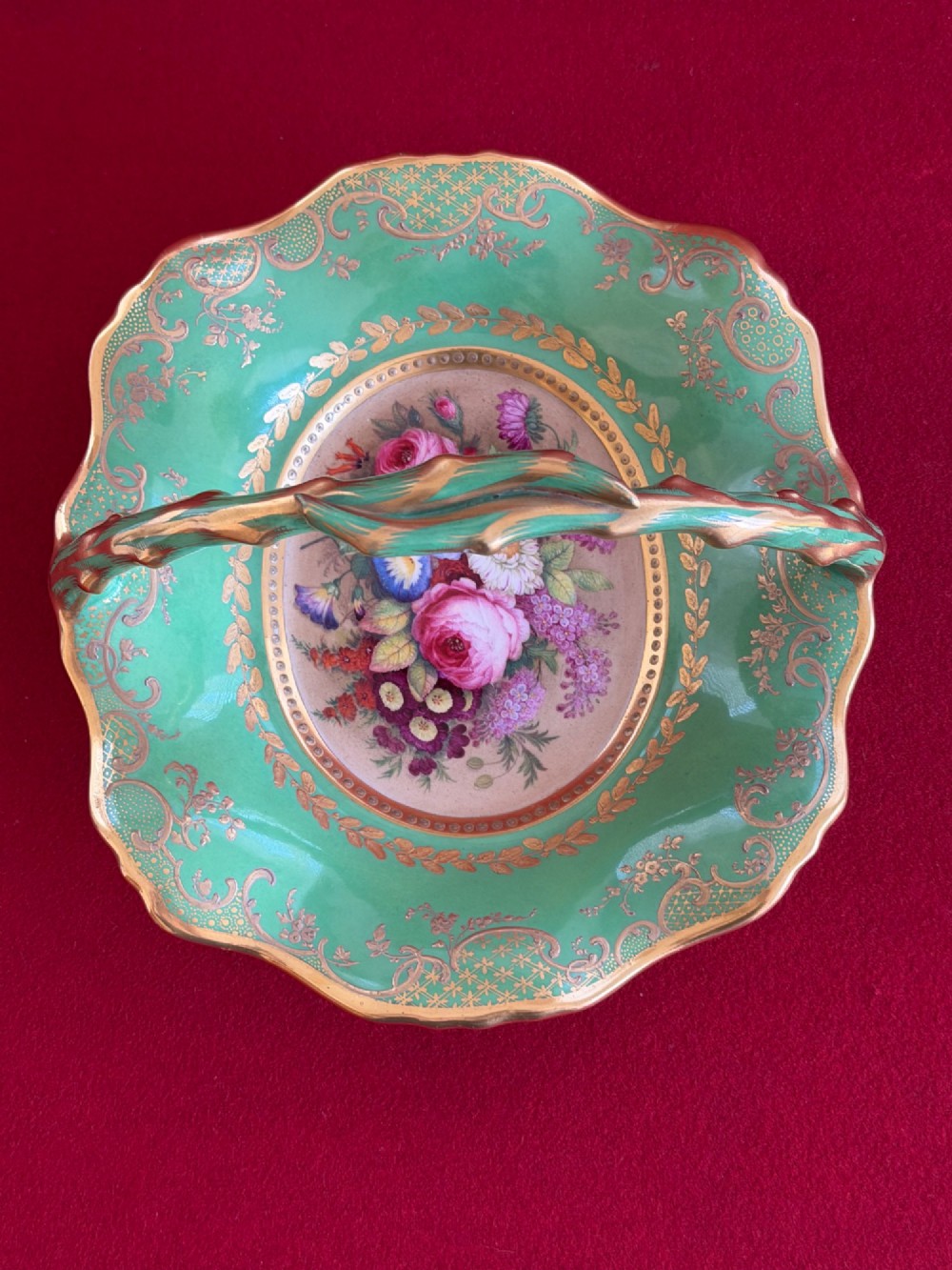 An antique green porcelain basket featuring a central hand-painted floral bouquet, gilt scrolling filigree, and a gilded branch handle. View IV
