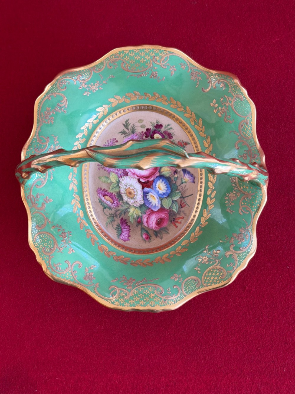 An antique green porcelain basket featuring a central hand-painted floral bouquet, gilt scrolling filigree, and a gilded branch handle. View V