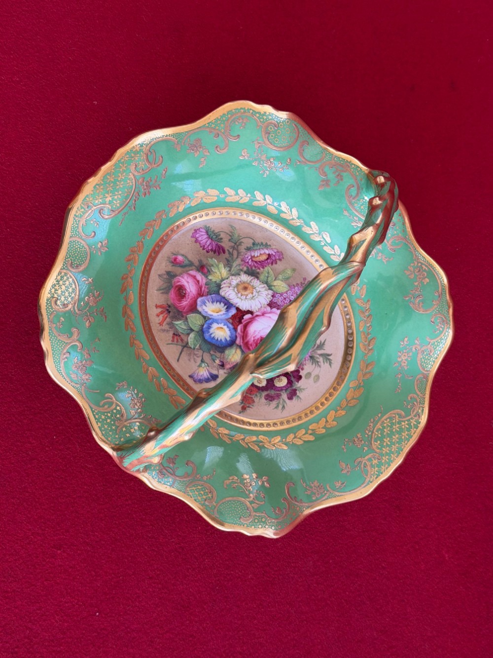 An antique green porcelain basket featuring a central hand-painted floral bouquet, gilt scrolling filigree, and a gilded branch handle. View VI