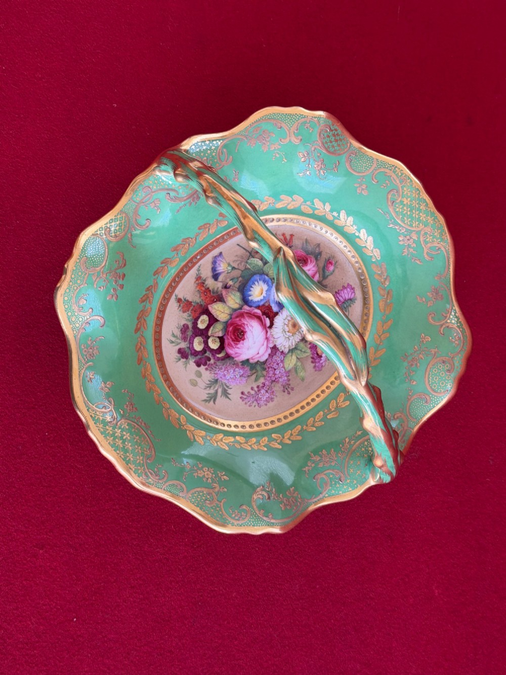 An antique green porcelain basket featuring a central hand-painted floral bouquet, gilt scrolling filigree, and a gilded branch handle. View VII