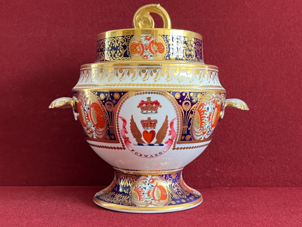 A Regency period porcelain sauce tureen with lid, decorated with cobalt blue and orange Imari patterns, gold gilding, and an armorial crest bearing the motto Forward.