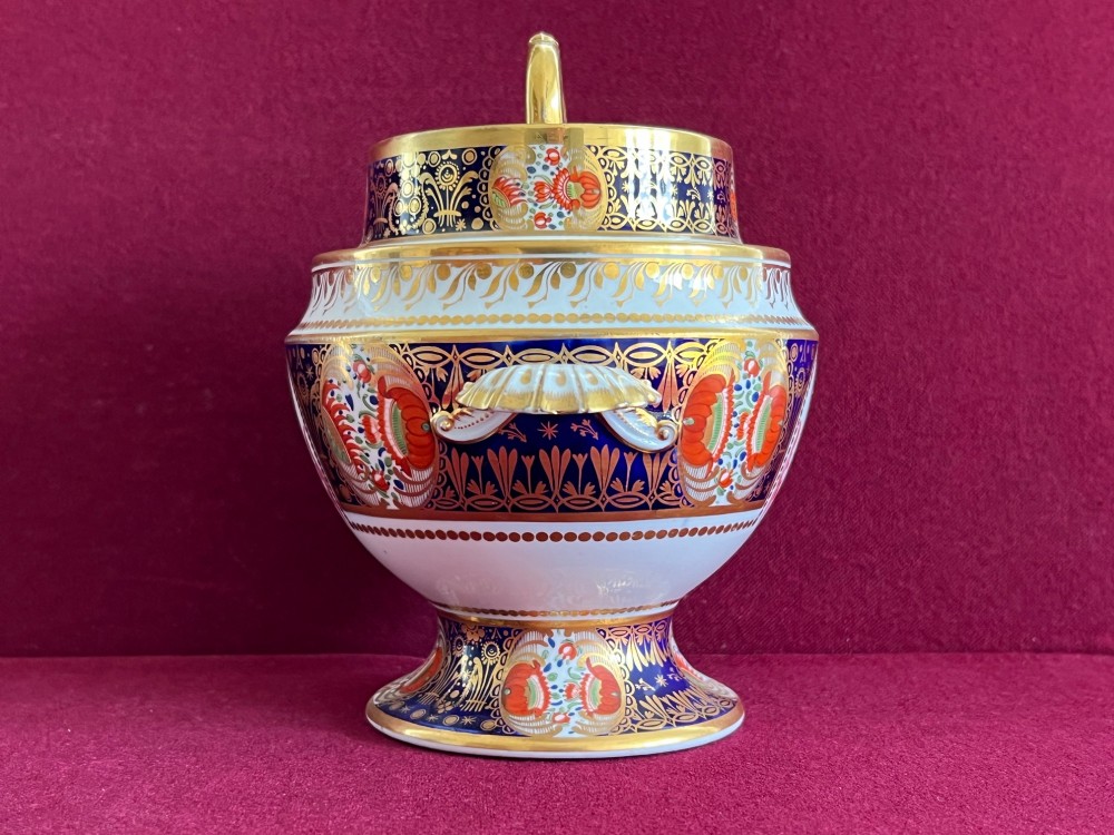A Regency period porcelain sauce tureen with lid, decorated with cobalt blue and orange Imari patterns, gold gilding, and an armorial crest bearing the motto Forward. View II
