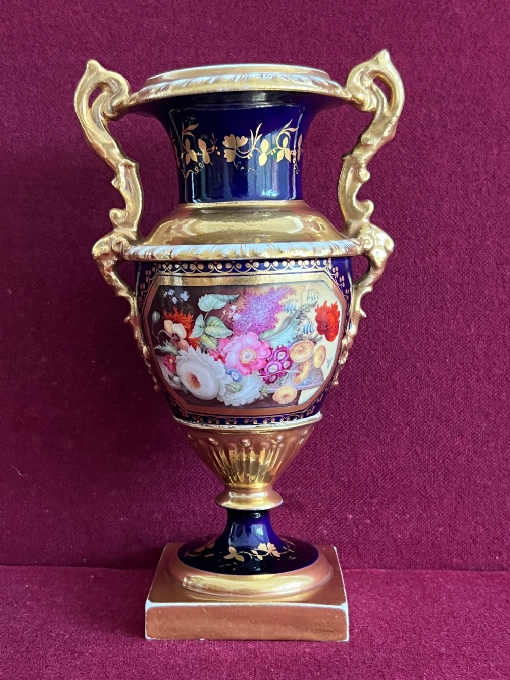 A three-piece set of cobalt blue and gilded Minton porcelain urn vases featuring hand-painted floral panels on square plinths. View II