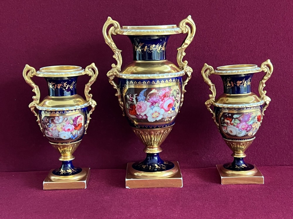 A three-piece set of cobalt blue and gilded Minton porcelain urn vases featuring hand-painted floral panels on square plinths. View III