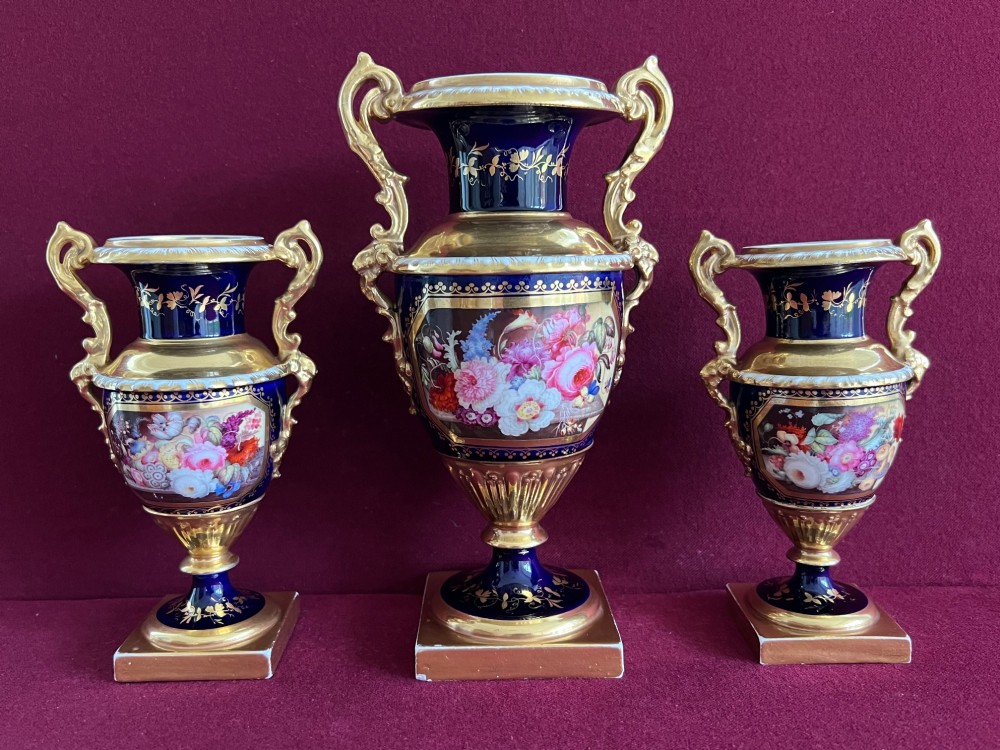 A three-piece set of cobalt blue and gilded Minton porcelain urn vases featuring hand-painted floral panels on square plinths. View IV